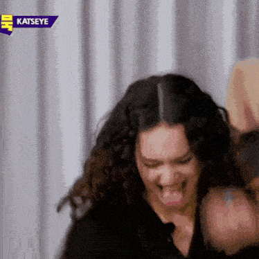 a woman with curly hair is making a funny face in front of a sign that says katseye .