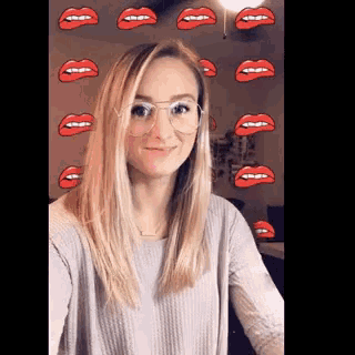 a woman wearing glasses is taking a selfie in front of a wall with red lips on it .