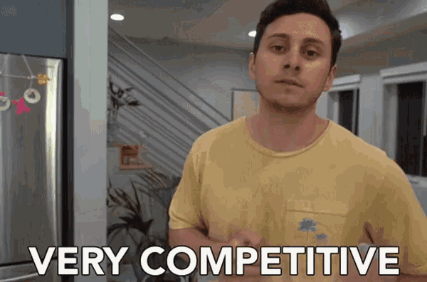 a man in a yellow shirt says very competitive in front of a refrigerator