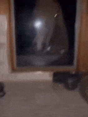 a blurry picture of a person standing in front of a window with a light shining through it .