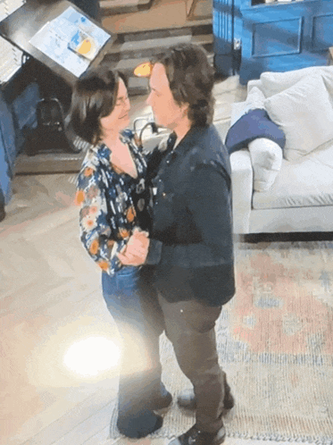 a man and woman are dancing in a living room with a couch in the background