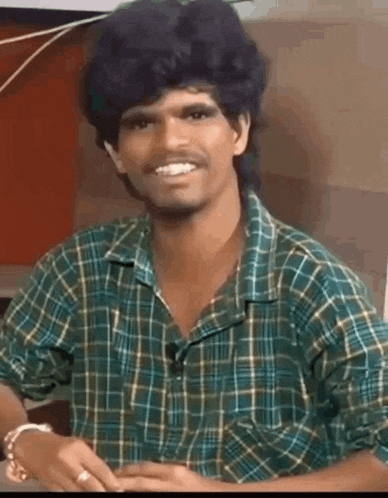 a man wearing a plaid shirt and a wig is smiling and looking at the camera .