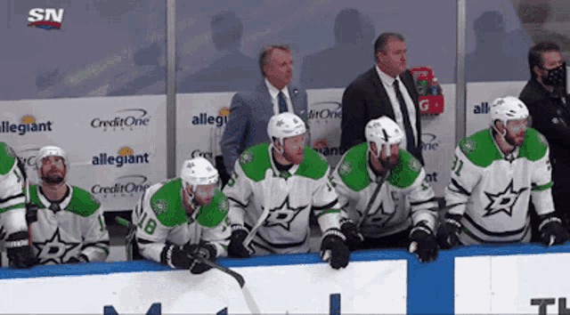 a group of hockey players are sitting on a bench in front of advertisements for allegiance and creditone