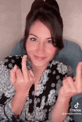 a woman wearing a black and white paisley shirt is making a heart with her fingers