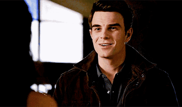a man in a brown jacket smiles while looking at a woman