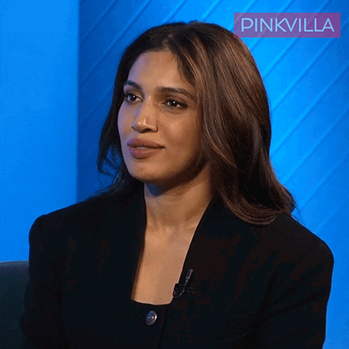 a woman in a black jacket is sitting in front of a blue wall with pinkvilla written on it