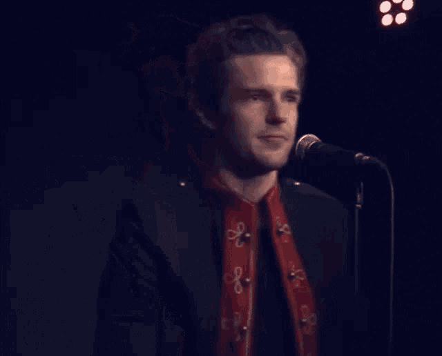 a man singing into a microphone wearing a red and gold jacket with the letter o on it