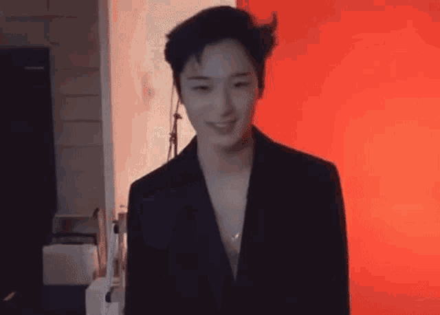 a young man in a black suit is standing in front of a red wall .
