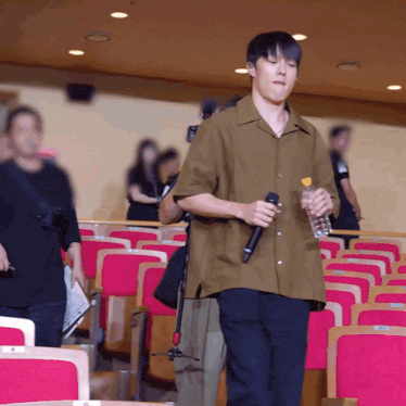 a man is holding a microphone and a bottle of water in an auditorium