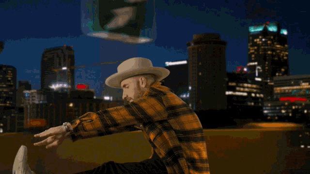 a man in a plaid shirt and hat sits on the roof of a car
