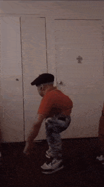 a man wearing a red shirt and a black hat is squatting in front of a white door .
