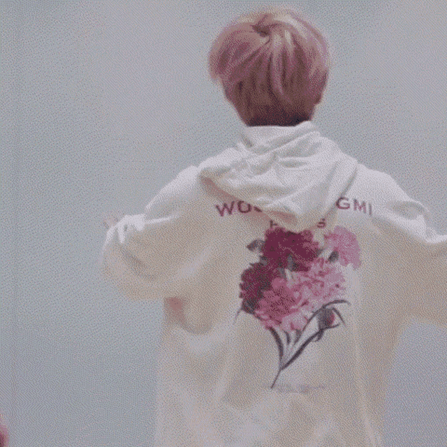 a person wearing a white hoodie with flowers on the back is dancing in a room .