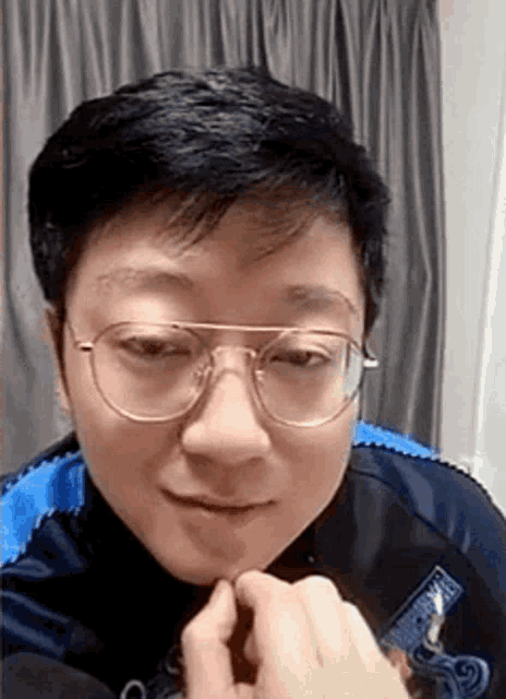 a man wearing glasses is making a funny face while sitting in front of a curtain .