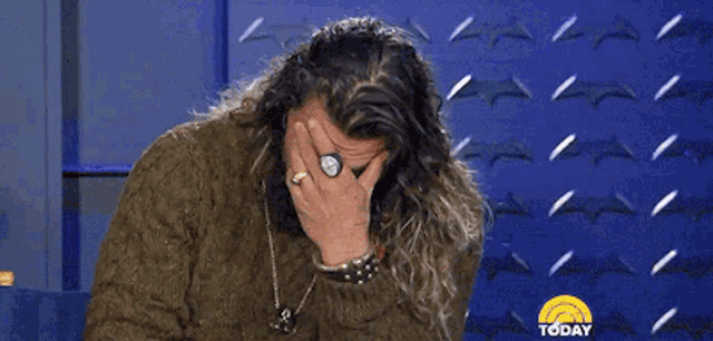 a man with long hair and a ring is covering his face with his hand .