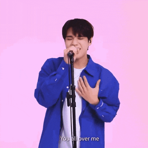 a man in a blue shirt is singing into a microphone with the words " you all over me " below him