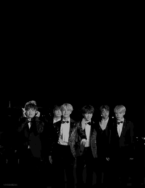 a black and white photo of a group of young men in tuxedos standing next to each other .