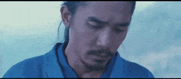 a man with a ponytail and beard is wearing a blue shirt
