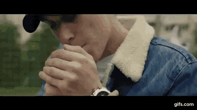 a man in a denim jacket is smoking a cigarette while wearing a watch .