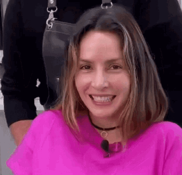 a woman in a pink shirt is smiling while sitting in front of a man in an apron .