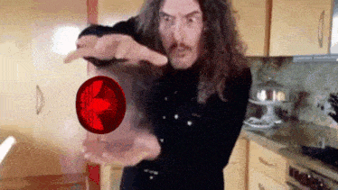 a man with long hair is pointing at a red object in his hands