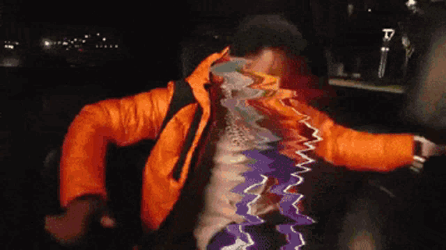 a man in an orange jacket is dancing with a purple and blue background