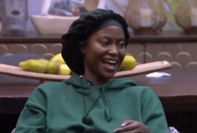 a woman wearing a green hoodie and a black hat is laughing .