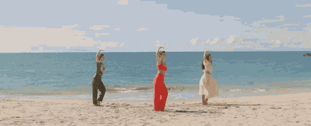 three women standing on a beach with their arms outstretched in front of the ocean