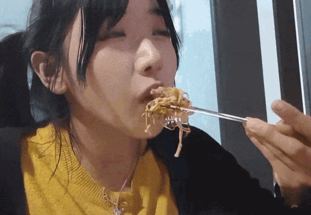 a woman in a yellow sweater is eating noodles with a fork
