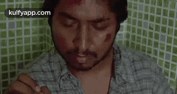 a man with blood on his face is sitting in front of a tiled wall .