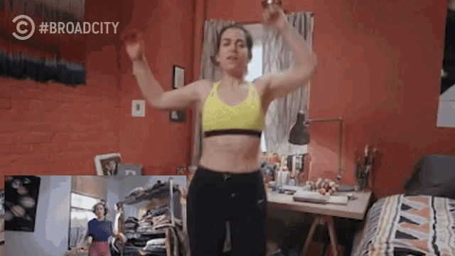a woman in a yellow sports bra is dancing in a bedroom with a broad city logo in the corner