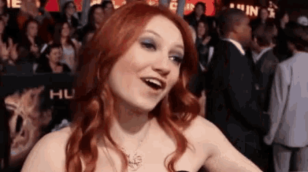 a woman with red hair is standing in front of a crowd with a sign that says hu on it