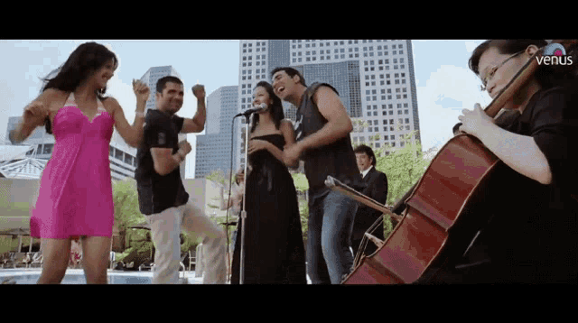 a group of people are singing and dancing in front of a man playing a cello and a woman singing into a microphone