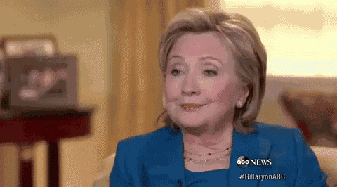 hillary clinton is smiling while sitting on a couch in front of a window .