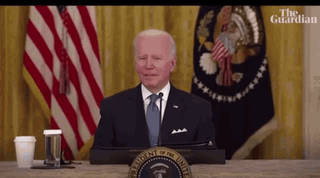 a man in a suit and tie is sitting at a podium in front of a podium with the presidential seal on it .