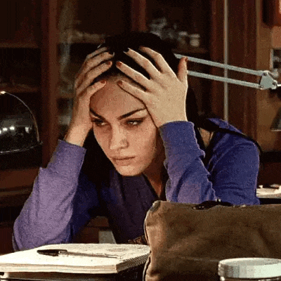 a woman is sitting at a desk with her hands on her head and a lamp .