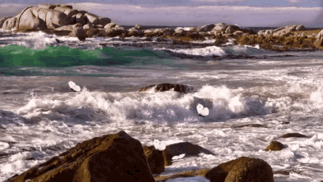 waves crashing against a rocky shoreline with a blue sky