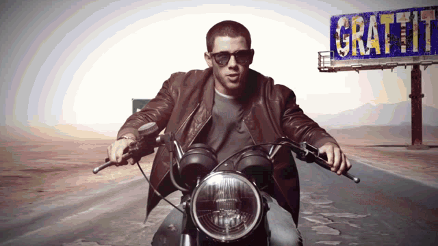 a man riding a motorcycle in front of a billboard that says graffitti
