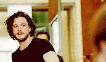 a man with curly hair and a beard is wearing a black shirt and looking at the camera .