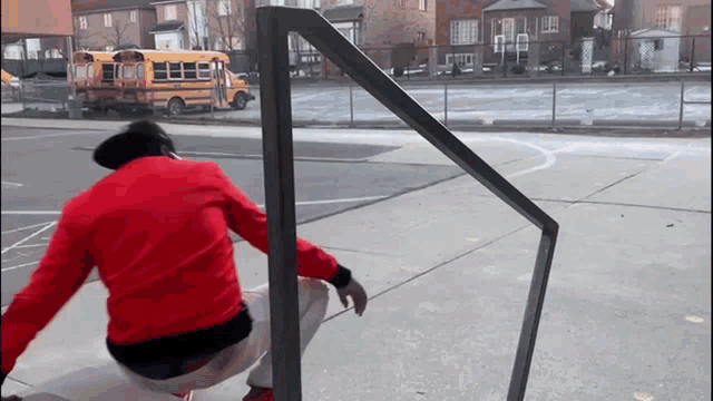 a man in a red jacket is squatting down in front of a yellow bus