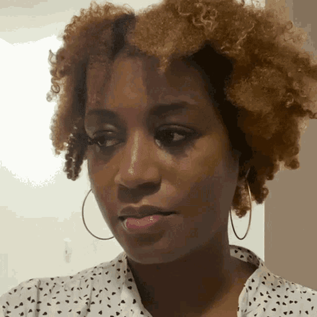 a woman with curly hair is wearing hoop earrings and a polka dot shirt