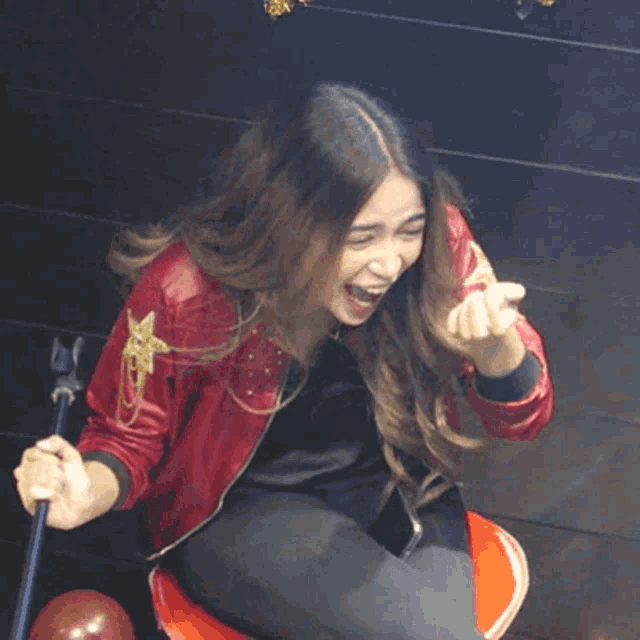 a woman in a red jacket is sitting on a red chair with her mouth open