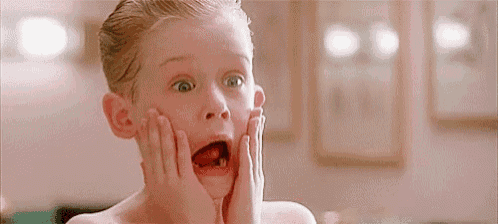 a young boy is making a surprised face while holding his face in his hands .