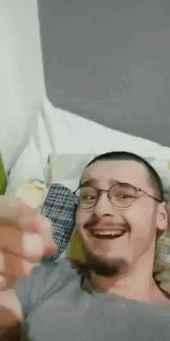 a man with glasses and a beard is smiling while laying on a bed .