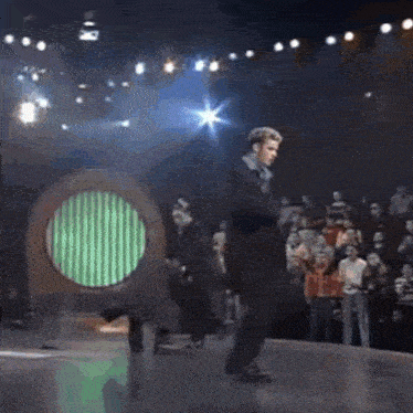 a man in a suit is dancing on a stage in front of a crowd