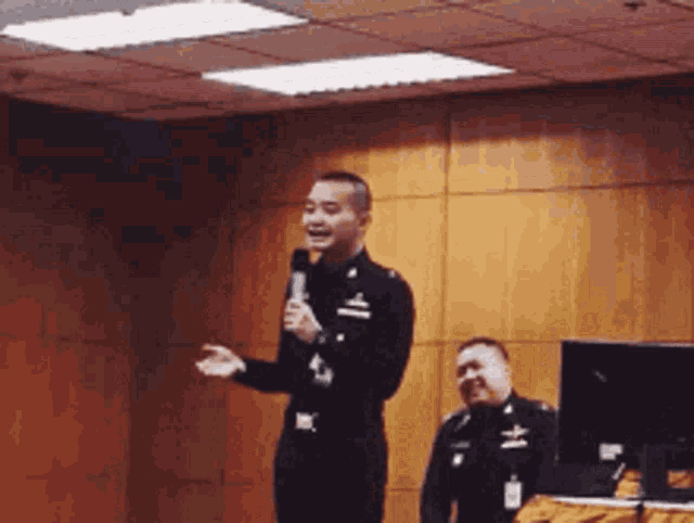 a man in a black uniform is holding a microphone while another man looks on