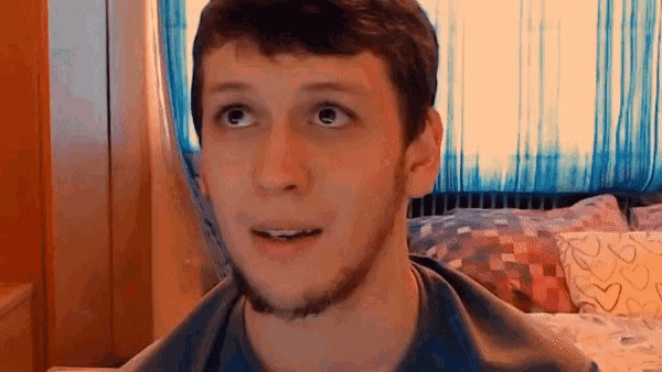a young man with a beard and a blue shirt looks up at something