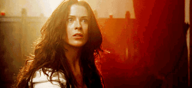 a woman with long hair is looking at the camera with a red background behind her