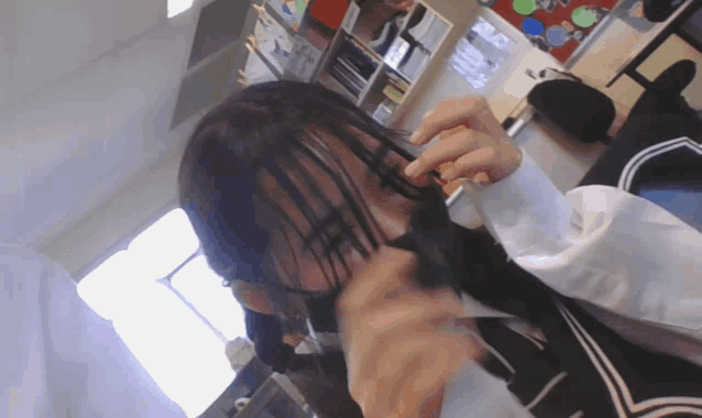 a girl is cutting her hair with a pair of scissors in a room