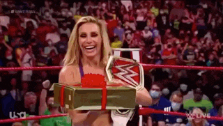 a woman is holding a gift box in a wrestling ring while smiling .