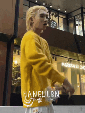 a man in a yellow sweater is standing in front of a building that says marks and spencer